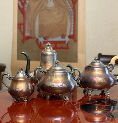a silver tea set sitting on a table in front of a painting