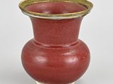 a red vase with a gold rim sitting on a white surface