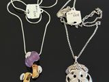 two silver necklaces with charms and a tag on a black surface