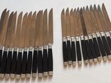 Plusieurs couteaux sont alignés sur une surface blanche, avec des manches noirs.