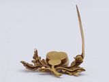 a small gold object with a leaf on it