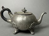 a silver teapot with a handle on a gray surface