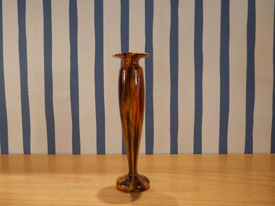 un vase marron posé sur une table en bois devant un mur rayé