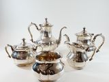 four pieces of silver tea and coffee set on a white surface