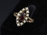 a close up of a gold ring with a red stone and pearls
