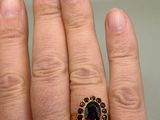a woman ' s hand holding a ring with a red stone on it