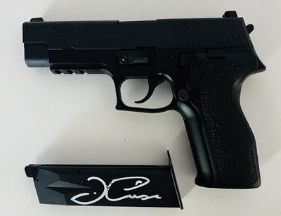 un pistolet noir sur lequel figure une signature, à côté d'un paquet de cigarettes