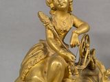 a gold clock with a woman sitting on top of it