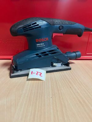 une ponceuse orbitale Bosch posée sur une table, à côté d'une boîte rouge