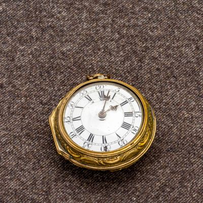 une petite horloge en or avec des chiffres romains