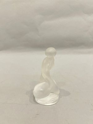 a glass figurine of a woman sitting on a white surface