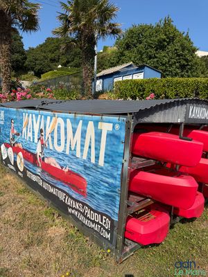 un grand panneau indiquant « Kayakmat » à côté d'une rangée de canoës