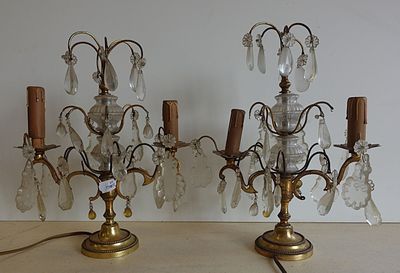 une paire de chandeliers anciens en laiton et cristal posés sur une table en bois