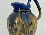 un vase bleu et marron muni d'une anse, posé sur une surface blanche