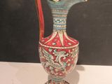 a red and blue vase with a gold handle on a white table
