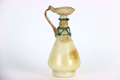 un petit vase en verre muni d'une anse, posé sur une surface blanche