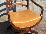 a wooden chair with a leather seat sitting on a sidewalk