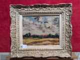 une peinture à l'huile représentant un paysage, dans un cadre argenté, posée sur une table