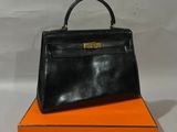 sac à main en cuir noir posé sur une boîte orange sur fond blanc