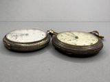 two silver pocket watches sitting side by side on a table