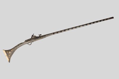 un vieux pistolet avec une crosse en bois sur fond gris
