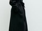 the woman is wearing a black coat and boots standing in front of a white wall