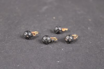 un gros plan sur quatre boucles d'oreilles à clous noires et dorées posées sur une surface noire