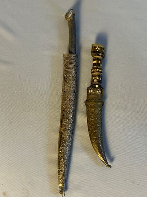 paire de couteau et de poignard plaqués or posés sur un tissu blanc