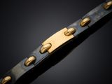 a close up of a metal bracelet with gold rivets on a black background
