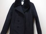 Le manteau est noir et est orné d'un col en fourrure.