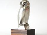 une image représentant une statue de chouette en argent posée sur un socle en bois