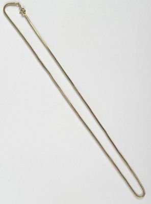 un collier en or avec une longue chaîne posé sur une surface blanche