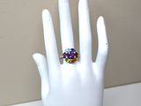 une main blanche tenant une bague sertie de pierres multicolores