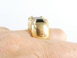 a person ' s hand holding a gold ring with a black stone