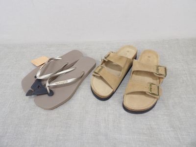 two pairs of sandals on a bed with a tag on them