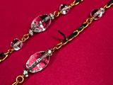 a close up of a pair of pink and black glass beads on a gold chain