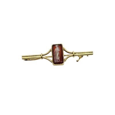 a close up of a gold tie bar with a red stone on it