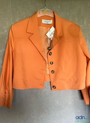 une veste orange suspendue à un cintre accroché au mur, avec une étiquette dessus