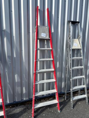 Plusieurs échelles sont alignées contre un mur métallique devant un immeuble.