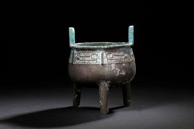 an old bronze pot with a handle sitting on a wooden stand