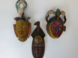 trois masques en bois accrochés au mur d'une pièce blanche