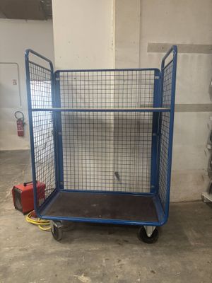 une grande cage bleue munie de roulettes, dans un entrepôt