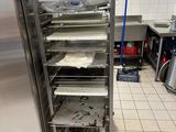 Plusieurs plateaux de nourriture sont empilés sur une étagère métallique dans une cuisine
