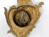 a gold clock hanging on the wall with a white background