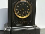 a black clock sitting on the floor in front of a white wall