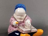 une figurine représentant une femme assise par terre en train de lire un livre