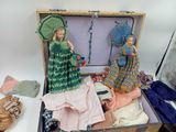 two dolls sitting inside of a suitcase with clothes on the floor