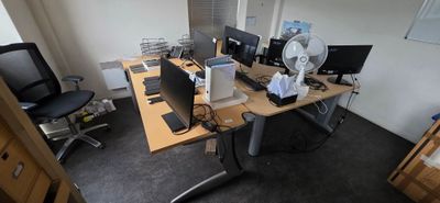 a desk with two computers and a fan in the corner
