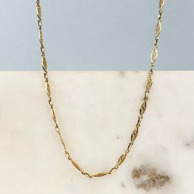 un collier à chaîne en or posé sur une surface en marbre