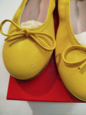 une paire de chaussons de danse jaunes posés sur une boîte rouge, elle-même posée sur une surface blanche